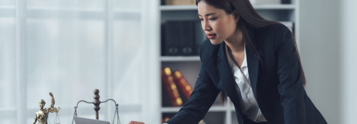 Anwaltskanzlei IT Recht: Juristin arbeitet am Laptop mit Justitia-Figur und Gesetzesbüchern im Hintergrund