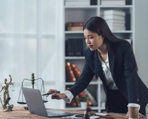 Anwaltskanzlei IT Recht: Juristin arbeitet am Laptop mit Justitia-Figur und Gesetzesbüchern im Hintergrund