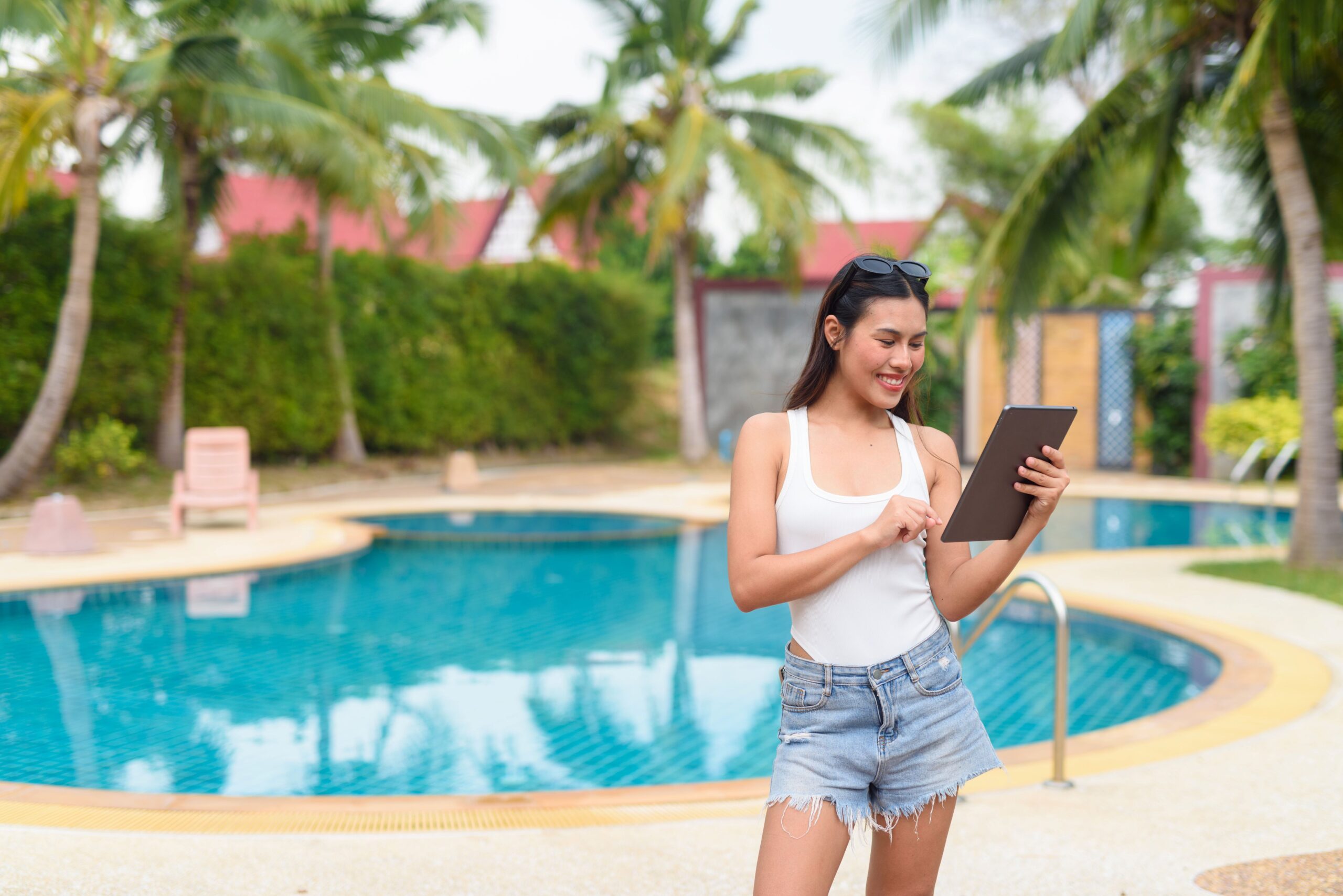 Frau steuert GFK Pool mit Tablet im Garten mit Palmen