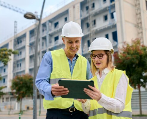 Zwei Bauleiter mit Schutzwesten und Helmen bei der Planung vor Rohbau mit Tablet