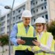 Zwei Bauleiter mit Schutzwesten und Helmen bei der Planung vor Rohbau mit Tablet