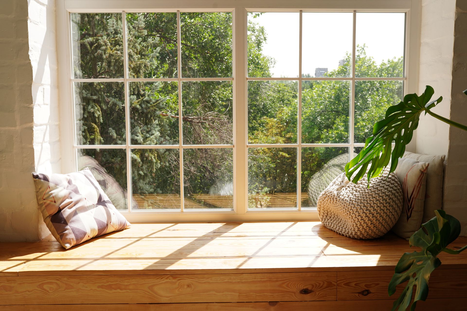 Sonnenlicht fällt durch große Fenster in einem Haus in Wuppertal, Sitzbank mit Kissen und Pflanzen betonen Wohnkomfort und Nachhaltigkeit.